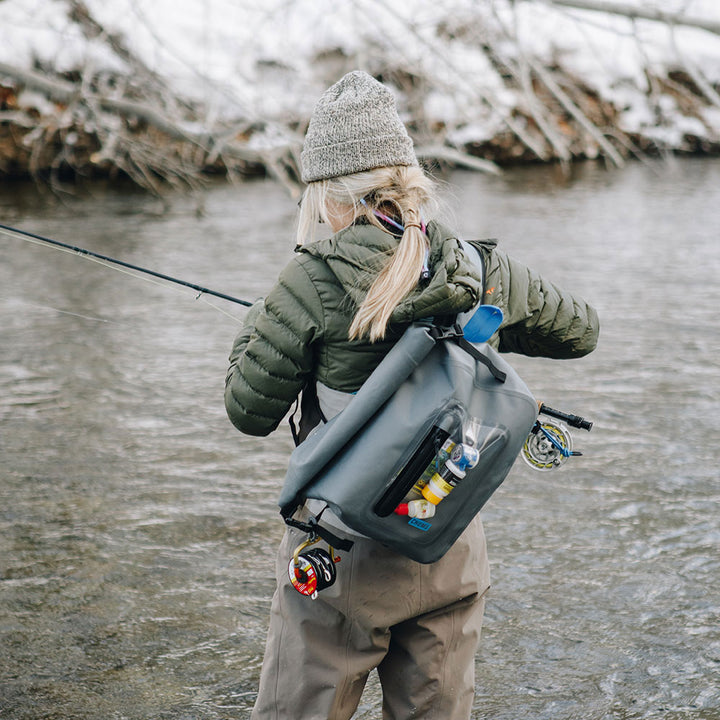 A woman fishing in a stream carrying a Rolltop Sling